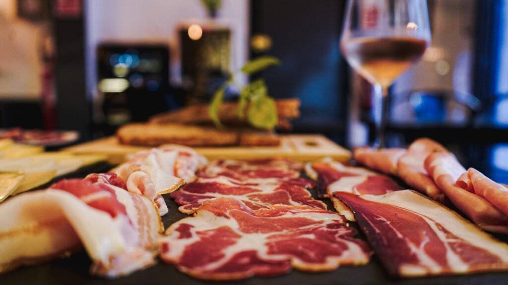 Food platter with sliced cold cuts, cheese and a glass of wine.